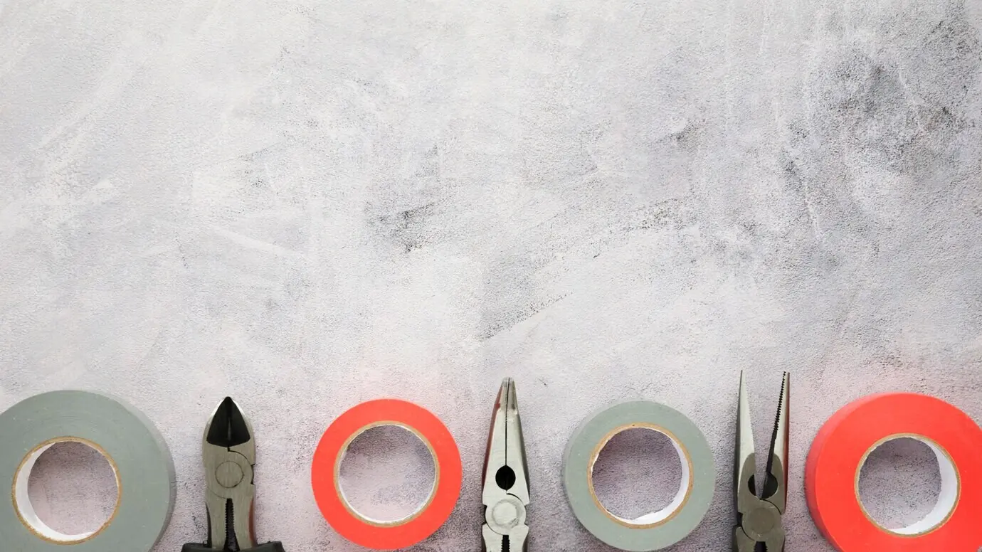 Isolierband und Zange in einer Reihe auf weißem Zementbetonboden angeordnet.